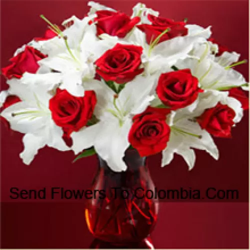 Punaiset ruusut ja valkoiset liljat joissa on hieman saniaisia lasimaljakossa